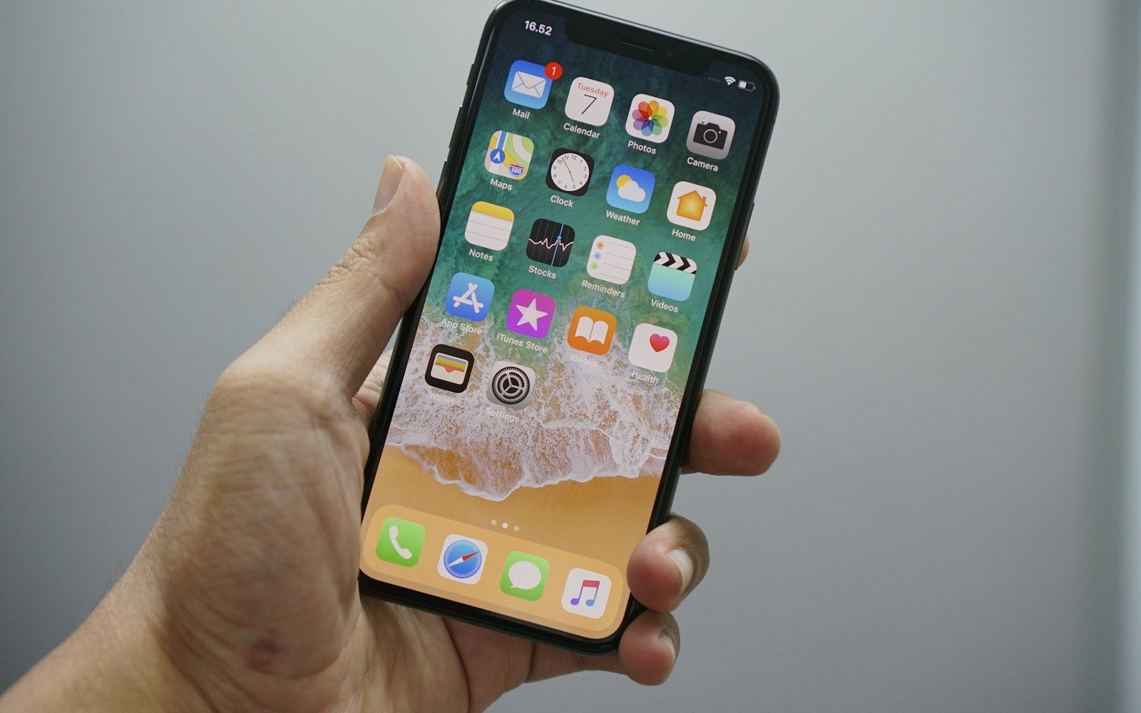 A hand holds a smartphone displaying a grid of app icons against a plain background.