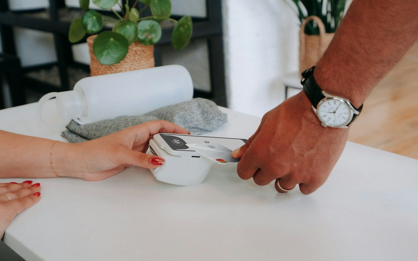 A customer taps a pale payment card on a handheld reader at a shop counter.