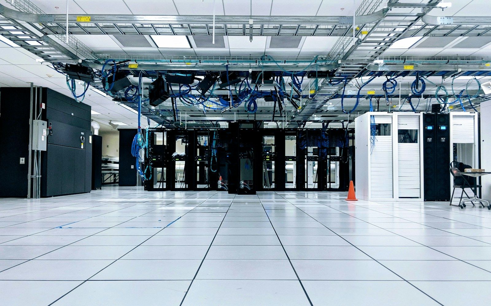 Server cabinets and overhead blue network cables in a bright data center.