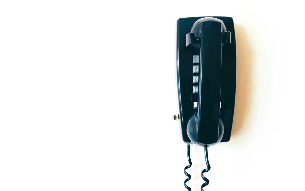 A black corded telephone mounted on a white wall.