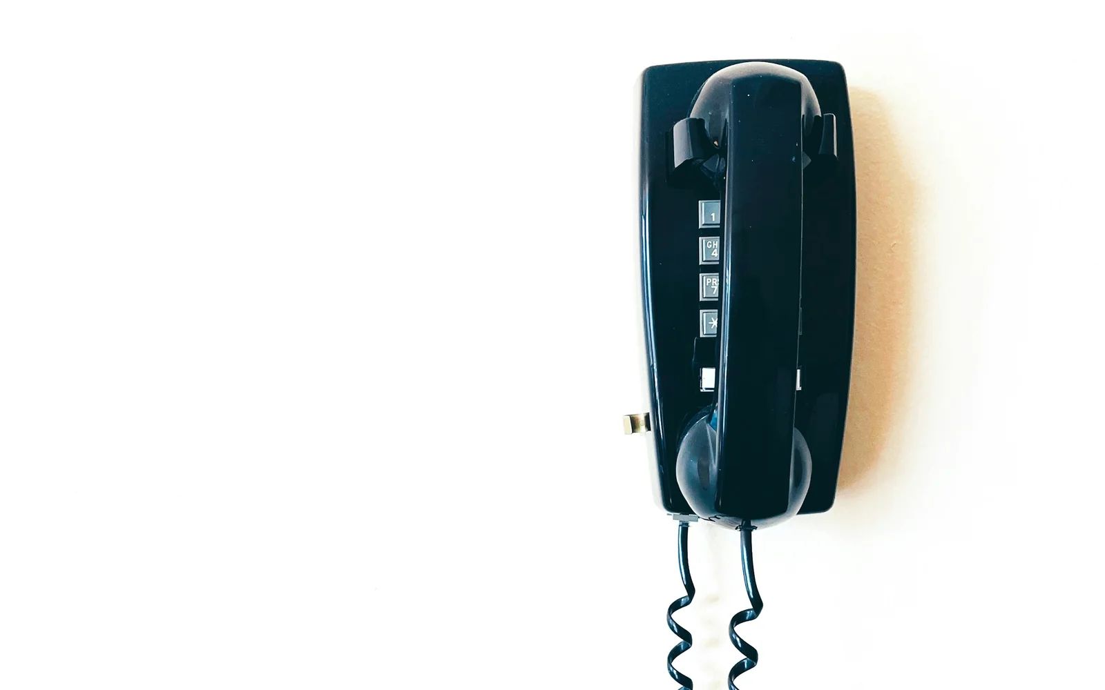 A black corded telephone mounted on a white wall.