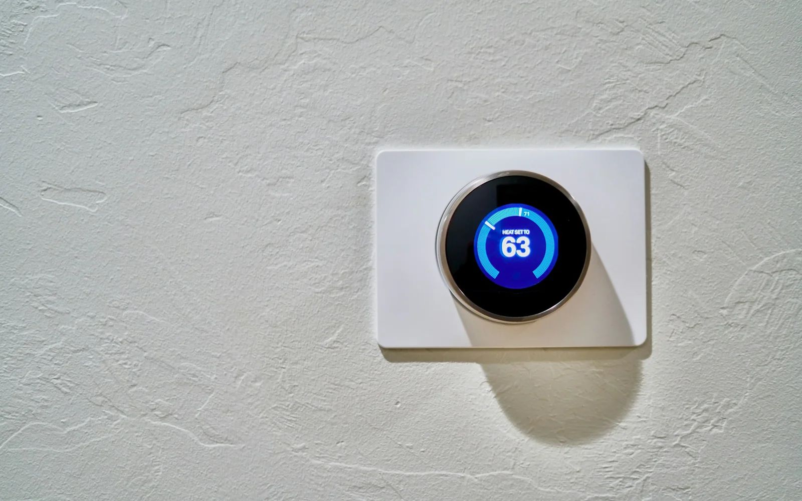 A round smart thermostat with a blue display mounted on a textured white wall.